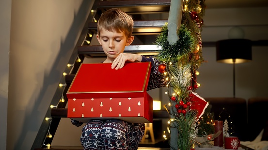 Little boy feeling upset and unhappy after opening Christmas gift box with present from Santa that he didn't want. Sadness, depression, solitude and negative emotions on winter holidays and New Year