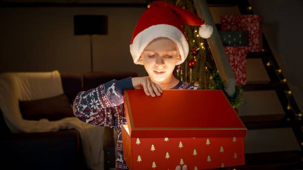 istock Excited little boy in Santa's hat opens magical glowing Christmas gift box with present on Christmas eve. Family celebrations on winter holidays 1791338016