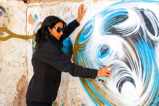 istock Woman in black spraying at a graffiti brick wall 179134036