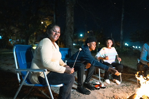 Portrait of mature woman roasting marshmallows with her family around a campfire