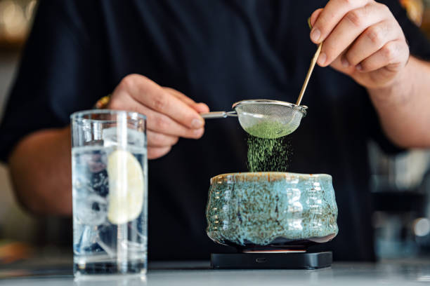 Hands of barista adding a spoon of powdered matcha tea in bowl