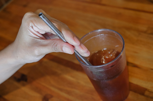 Close-up POV shot of unrecognizable female hand holding a stainless steel straw on her ice tea drink