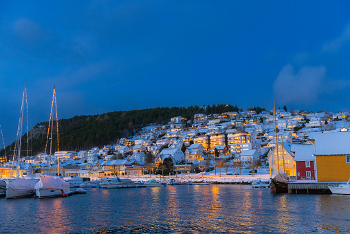 Majestic winter night over the boats on the reflection sea and buildings in Christmas lights in the authentic Scandinavian town Ulsteinvik during twilight