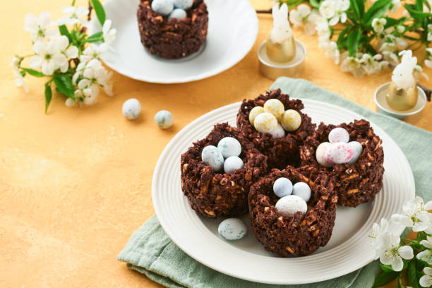 istock Easter chocolate nest cake with mini chocolate candy eggs with blossoming cherry or apple flowers on yellow background table. Creative recipe for Easter table with holiday decorations. Top view. 1791419963