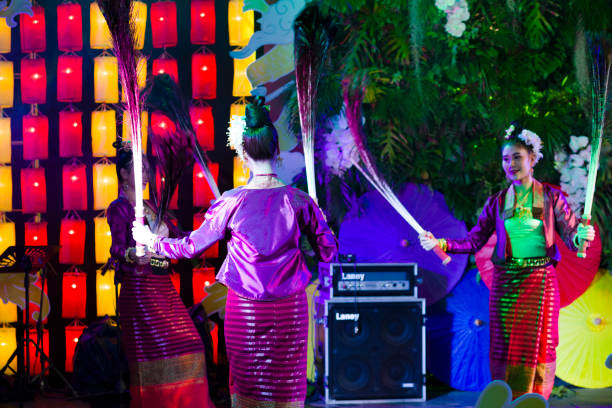 Female thai dance performance  with peacock feathers. Female thai dance performance  with peacock feathers. A group of young  thai women are dancing traditional performance in traditional costumes -  they are performing classical dance in public to people who visit square and night market  in Chiang Mai. All dancers are holding peacock feathers,  Scene is at One Nimman Square. Performance is on a small stage and they are dancing in public for people who are visiting market as part of several entertainment of dancers and singers true thailand classic stock pictures, royalty-free photos & images