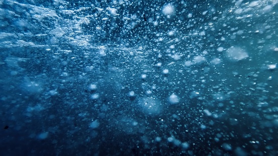 Underwater view on fast water stream with flowing air bubbles rising up to the sea surface.