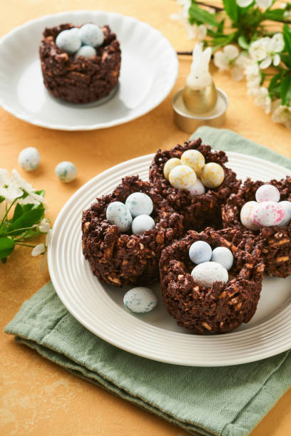 istock Easter chocolate nest cake with mini chocolate candy eggs with blossoming cherry or apple flowers on yellow background table. Creative recipe for Easter table with holiday decorations. Top view. 1791421037