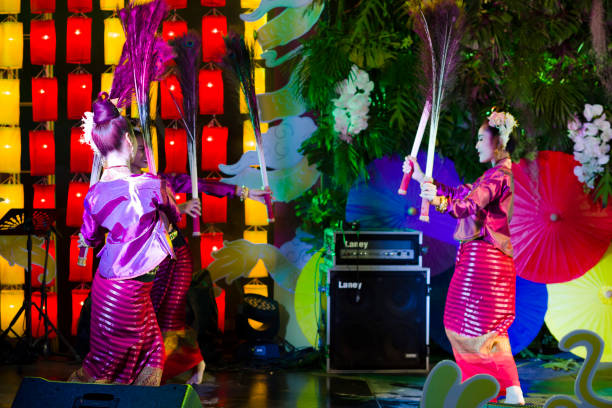 Portrait of elegant dressed  thai dancers moving in a circle holding peacock feathers. Portrait of elegant dressed  thai dancers moving in a circle holding peacock feathers. Classical   Rum Thai performance   with peacock feathers. Young  thai women are dancing traditional performance in traditional costumes. Scene is in public and for  people who visit square and night market  in Chiang Mai. They are dancing and moving in a circle and are changing positions. All dancers are holding peacock feathers,  Scene is at One Nimman Square. Performance is on a small stage and they are dancing in public for people who are visiting market as part of several entertainment of dancers and singers true thailand classic stock pictures, royalty-free photos & images