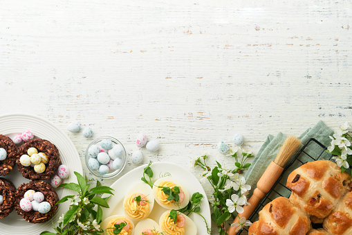 Easter brunch or breakfast. Easter chocolate nest cake with chocolate candy eggs, traditional hot cross buns and deviled eggs with bouquets of blooming apple trees. Spring Easter holiday food concept.