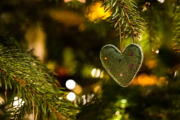 A fabric heart with decorations on the Christmas tree in atmospheric light for Christmas