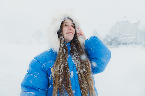 Portrait of a happy female wearing warm winter jacket walking in the town during strong winter blizzard contemplating Christmas time outdoors