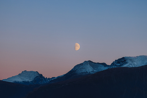 Dramatic view of the Moon in the twilight sky above the snowy mountain peaks of Norway, Scandinavia