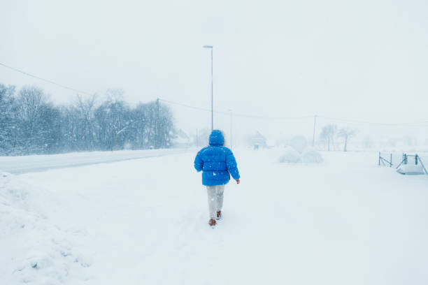 mulher no casaco azul admirando o inverno andando na rua na vila escandinava durante a queda de neve pesada - rear view winter blizzard nordic countries - fotografias e filmes do acervo