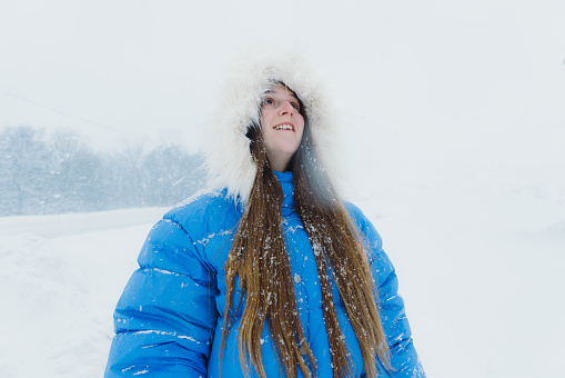 Young adult woman in a hat and yellow jacket breathing fresh air in the winter forest