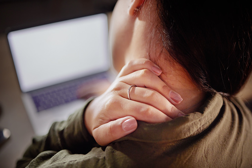 Neck pain, hand and woman with closeup at desk with laptop, stiff joint with injury and hurt. Burnout, muscle tension and anatomy with health mockup, female working with bad posture and injured