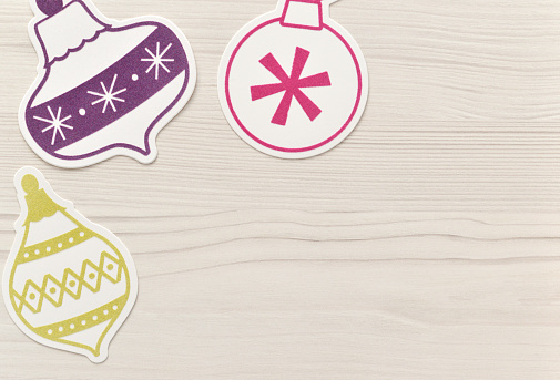 Closeup of generic paper Christmas ornaments on a whitewashed wood background.
