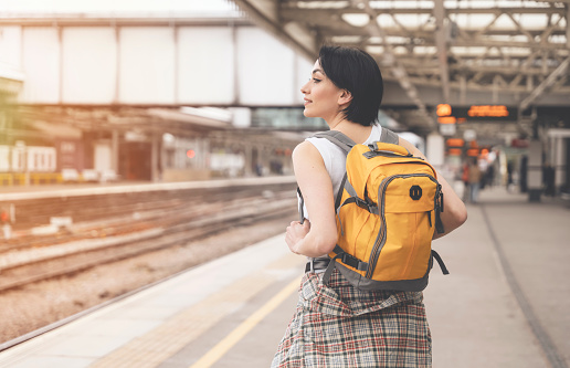 woman with backpack while at the train station and the train is arriving. Enjoying travel concept