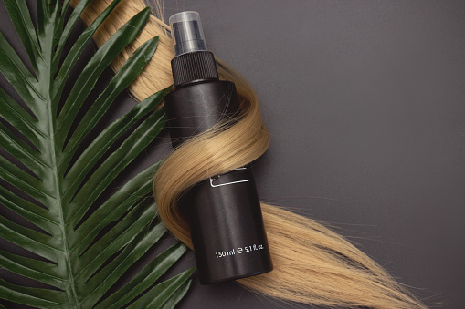 Blond shiny hair wave, Hair care spray and tropical leave on black background. Hairdresser service. Beauty salon service. Natural cosmetics for hair care. Hair care spa concept