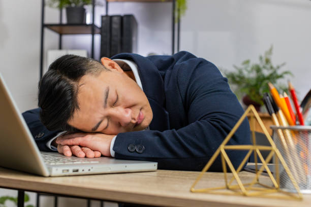 退屈な眠いビジネスマン労働者は、オフィスの机で眠りに落ちている手にもたれかかってラップトップで働いています - やる気が出ない ストックフォトと画像