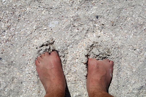 Man's feet on the beach sand, top view.