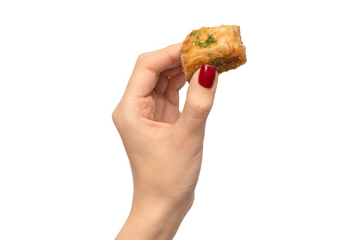 Delicious sweet baklava in woman hand with red nails isolated on a white background. Top view.