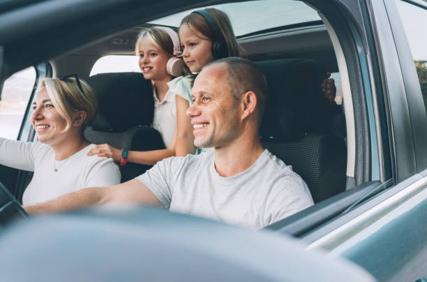 istock Happy young couple with two daughters inside the modern car with panoramic roof during auto trop. They are smiling, laughing during road trip. Family values, traveling concepts. 1791521898