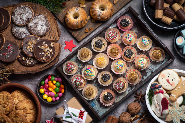 Christmas table full of colorful, delicious homemade sweets. There are white chocolate pralines, mini bundt cakes, colorful candies, gingerbread, marshmallow and various cookies