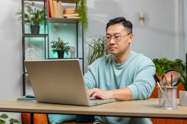 istock Confident concentrated Asian man working remotely on a project on laptop computer at home room 1791525332