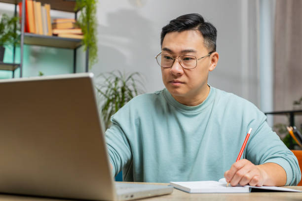 istock Asian man freelancer making notes on notebook at home, use laptop, prepare business financial report 1791525588