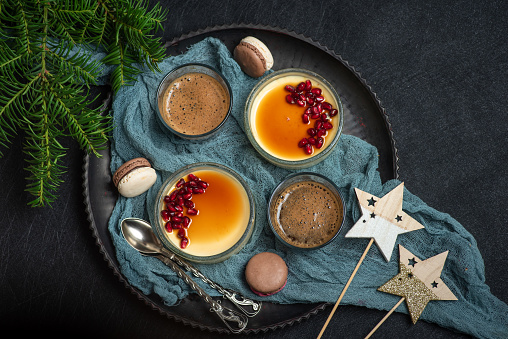 Creme brulee, colorful macaroons cookies and a cup of coffee. Traditional French dessert with vanilla cream in a glass bowl on a dark background, with a Christmas decoration