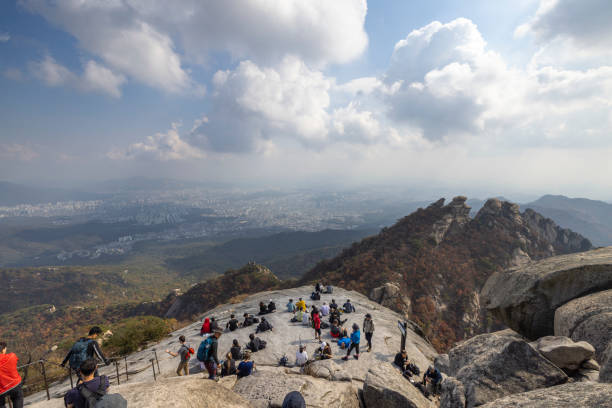seoul, south korea - october 23, 2023: people hiking and climbing to baegundae mountain and resting at the peak in bukhansan national park in seoul.