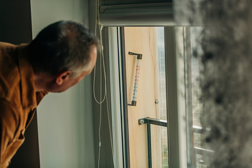 elderly man looks at the temperature on the outdoor thermometer through a window