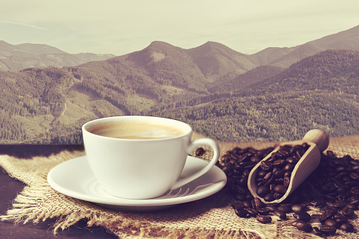 Cup of aromatic hot coffee on wooden table and beautiful view of mountain landscape
