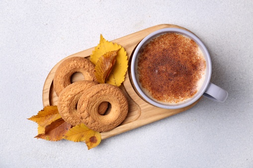 Cup of hot drink, cookies and autumn leaves on light grey textured table, top view