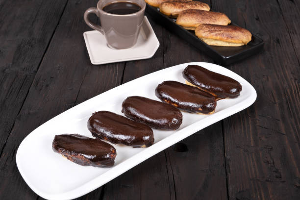 istock Chocolate eclair cakes on wooden background. Coffee cup next to it. 1791567334