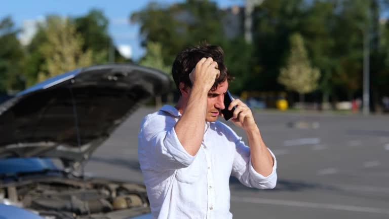 Upset man talking on mobile phone near broken car outdoors in the city. Car repair. Transport and lifestyle concept. Real time