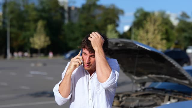 Unhappy man standing near his broken car with open hood and talking on mobile phone, calling emergency road service. Transport and lifestyle concept. Real time