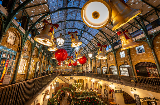 London, UK - Nov 8 2023: Covent Garden Market with Christmas decorations. Large bells and baubles hang from the roof. People are shopping and sitting in a cafe.