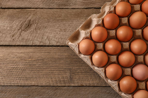 istock Fresh raw chicken eggs in carton on wooden table, top view. Space for text 1791584345