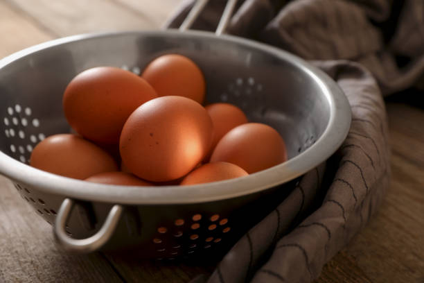 Chicken eggs in colander and napkin on wooden table