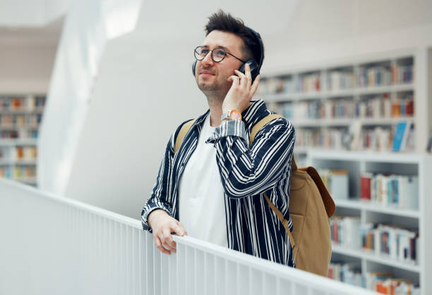 istock Headphones, college student man and university library work or research for learning. School campus building, music and live song streaming of a person looking for study books 1791586804