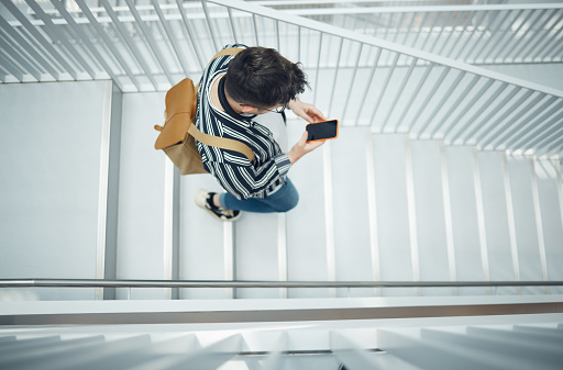 Phone, stairs and education with a student man walking down a staircase at university or college. Mobile, study and campus with a male pupil taking steps to get to class for learning or development