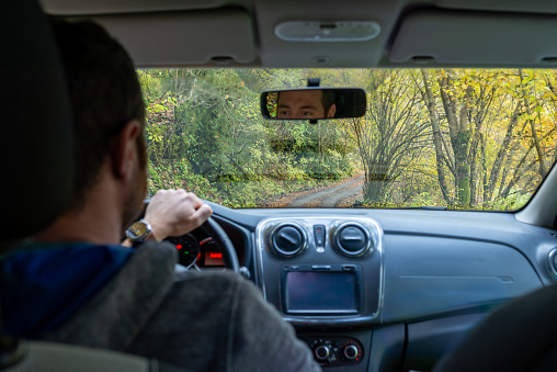 Rear view of a blurred man driving a car through an autumnal forest.