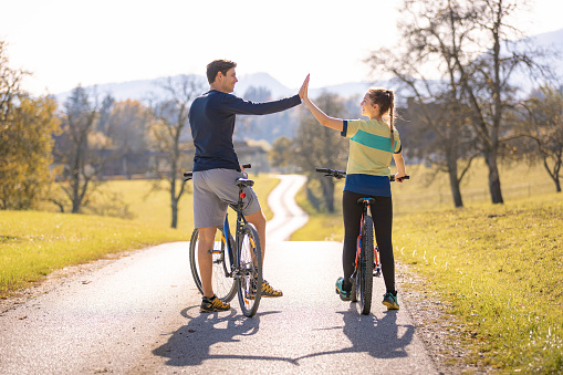 Cyclist couple giving high five while riding along the road in the beautiful, quiet countryside surrounding on a pleasant autumn day.