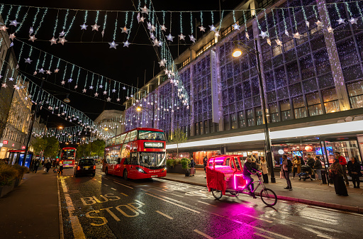 London, UK - Nov 8 2023: Oxford Street, a famous shopping street in Central London with Christmas lights. A pedicab and London bus are outside the John Lewis department store.