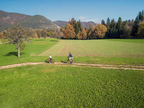 Two cyclists enjoying a ride along the road across green mountain pastures in an autumn season, aerial view. Active recreation and travel concepts.
