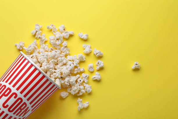 istock Overturned paper cup with delicious popcorn on yellow background, flat lay. Space for text 1791607466