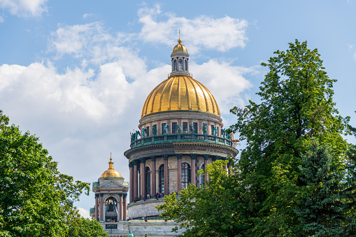 Close-up view of golden dome of Russian Orthodox Saint Isaac's Cathedral (or Isaakievskiy Sobor) between green trees in a sunny summer day in Saint Petersburg, Russia. Soft focus. Religion theme.
