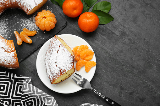 Piece of delicious homemade yogurt cake with powdered sugar and tangerines on gray table, flat lay. Space for text