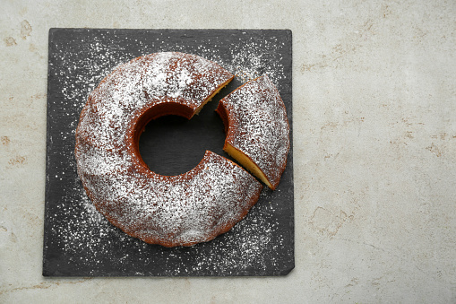 Homemade yogurt cake with powdered sugar on light grey table, top view. Space for text